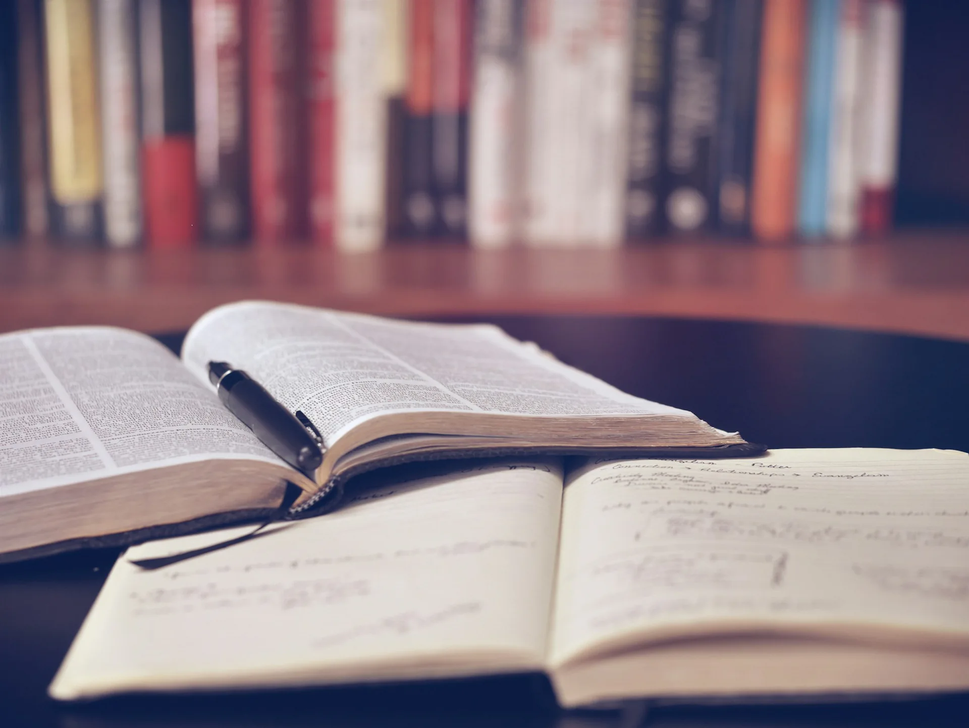 Open book and study notes Open textbook and handwritten notes on a desk in front of a bookshelf