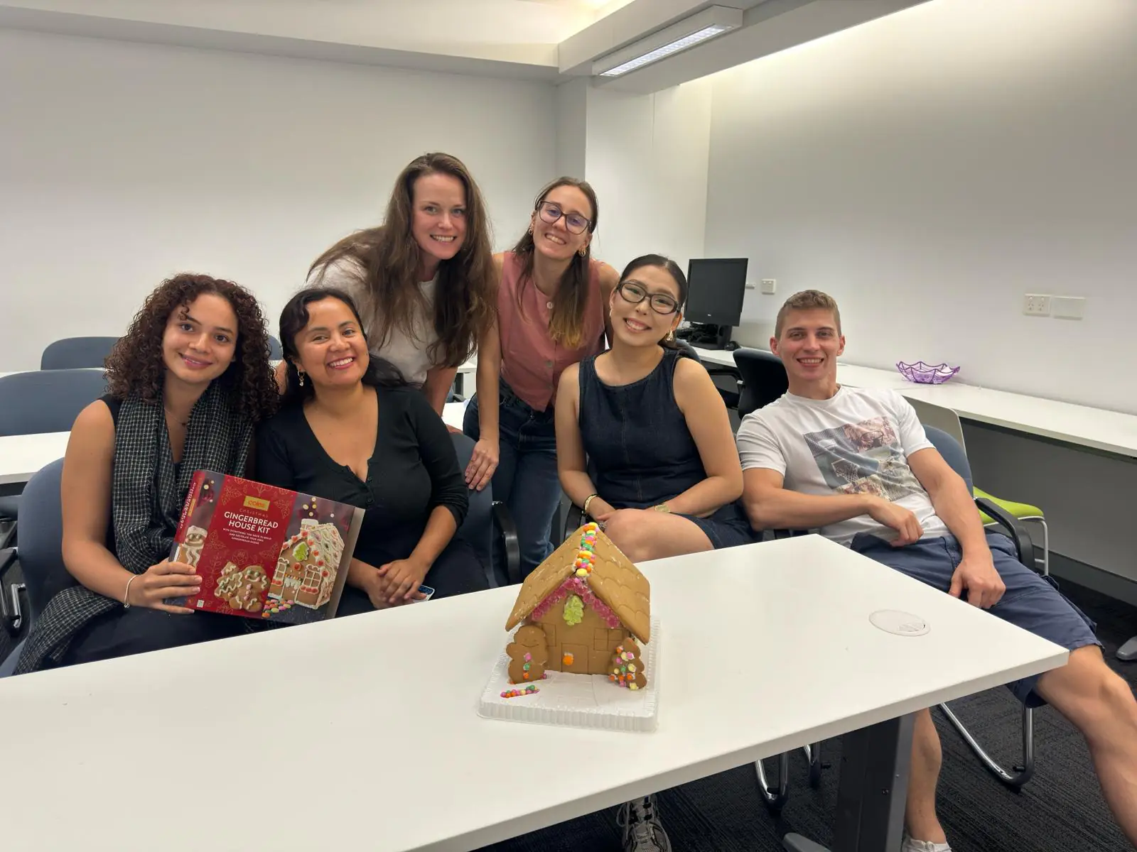Christmas celebration, 2025 Boston Institute students waving beside a gingerbread house at the Christmas party