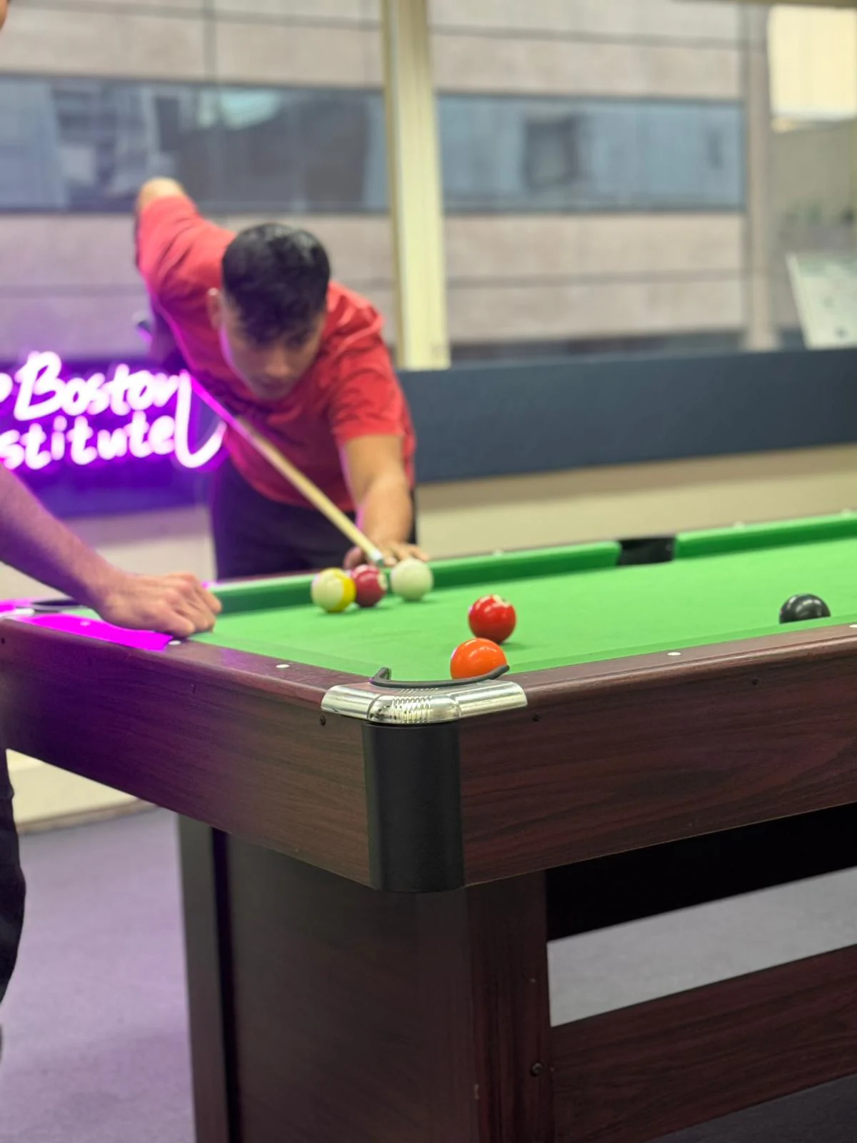 Pool match under neon sign, 2025 Student playing pool beneath a neon Boston Institute sign