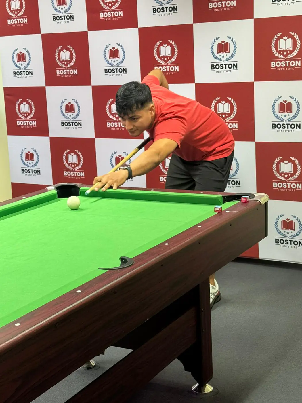 Pool match, 2025 Student playing pool in front of a Boston Institute branded backdrop