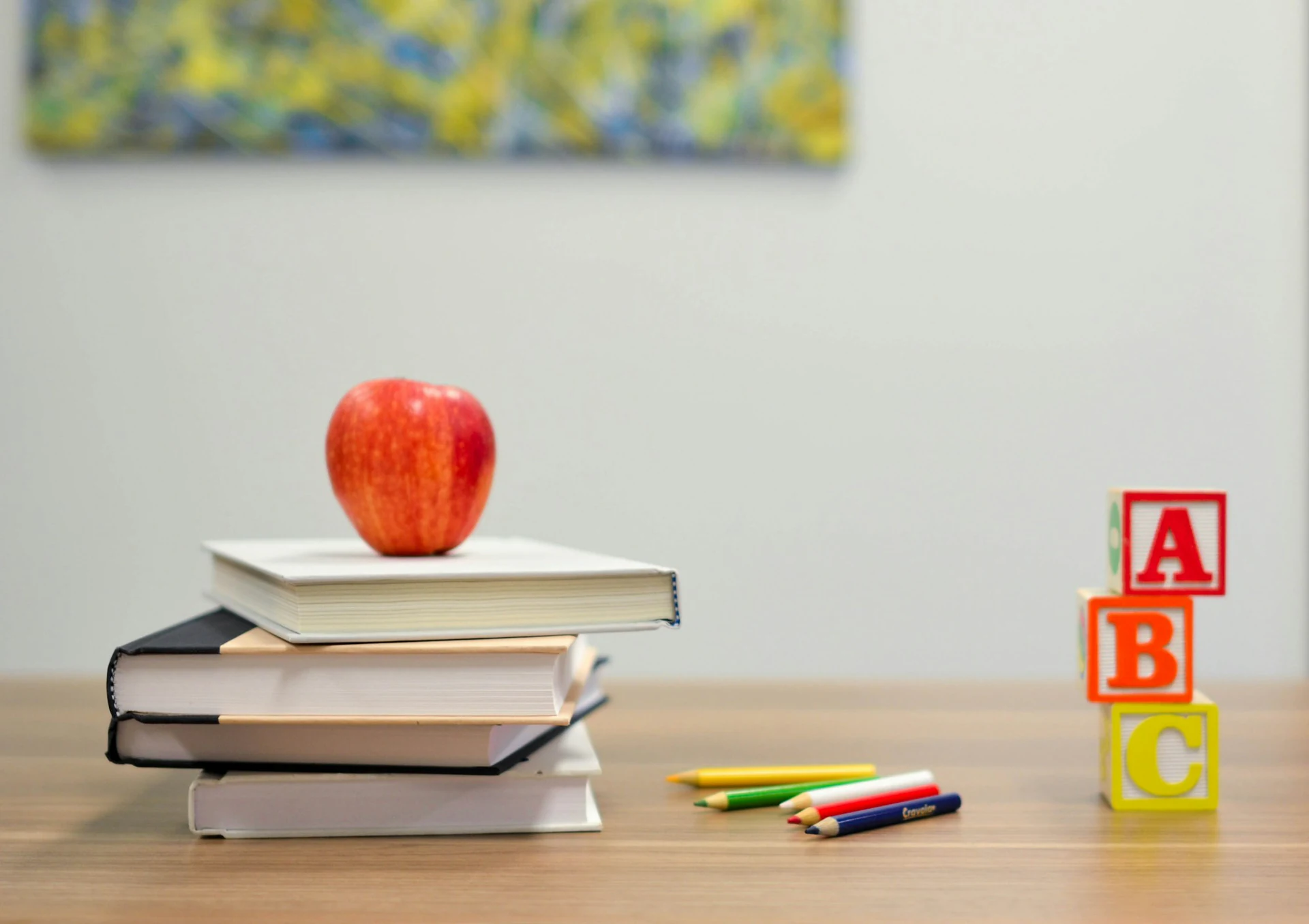 Stack of school books with an apple and alphabet blocks on a classroom desk