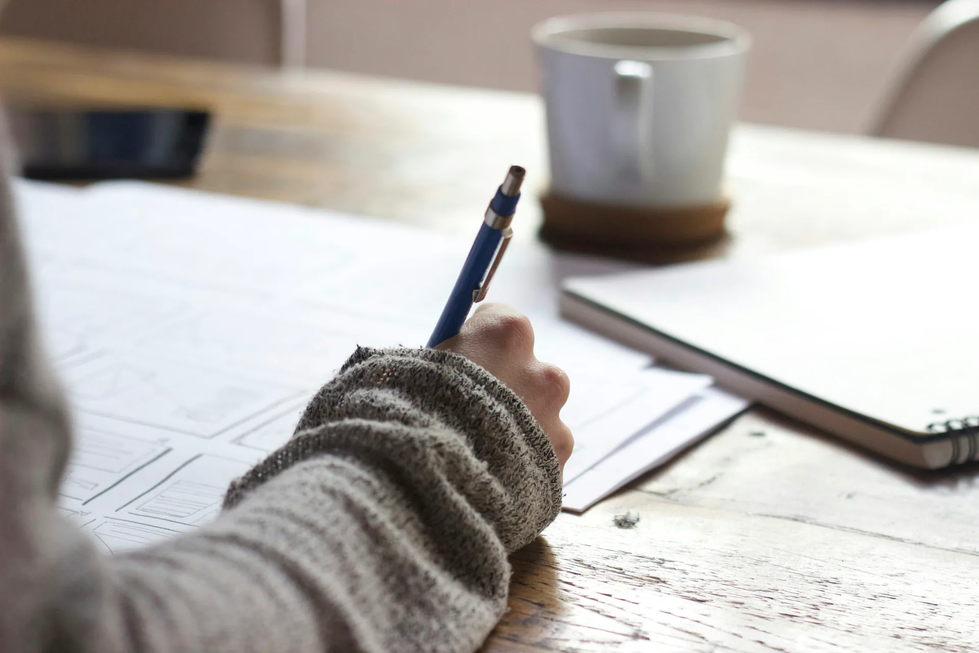 Close-up of a person writing study notes in a notebook beside a cup of coffee